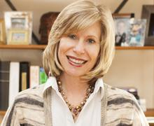 A woman in a striped cardigan standing in front of a bookshelf.